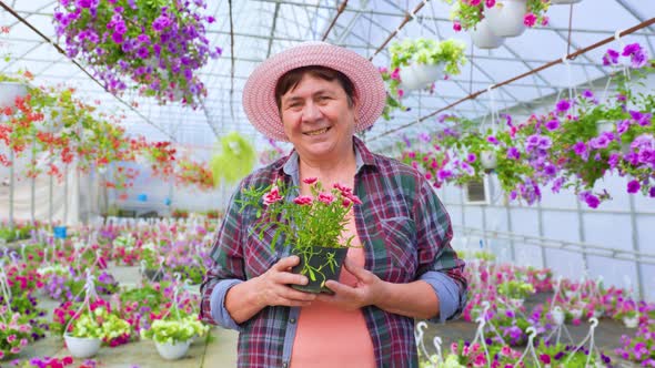 Front View Looking at Camera Florist Aged Woman Stands in Greenhouse Among Indoor Flowers in Pots