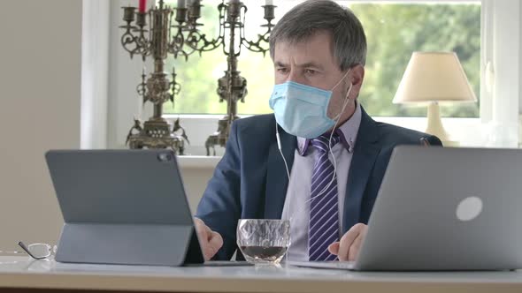 Confident Caucasian Businessman in Face Mask Sitting at the Table with Laptop and Tablet and