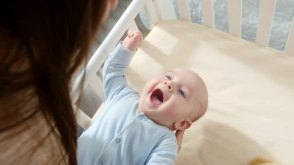 Happy Smiling Baby Boy Looking at Mother Rocking Him in Cradle