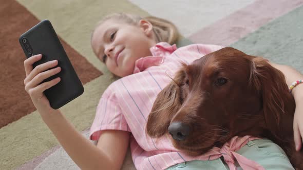 Girl Lying on Carpet with Smartphone and Dog