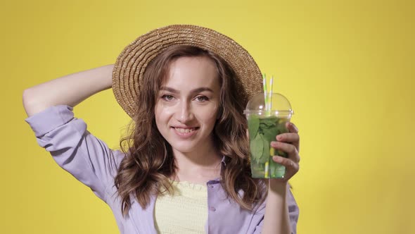 Surprised Woman Drink Mojito cocktail From Plastic Cup Over Yellow Studio Background