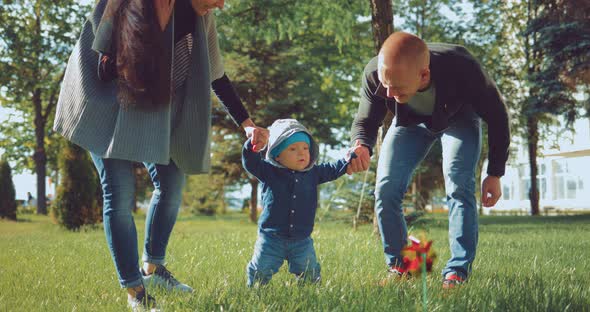 Young Parents Holding Her Young Child As He Practices His First Steps in the Park