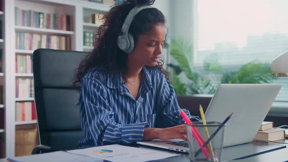 Young Indian Woman Listening to Music on Headphones and Working with Laptop