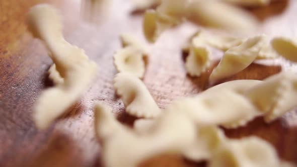 Bow tie pasta falling on a textured surface of rustic wooden bowl. Macro. Mediterranean cuisine