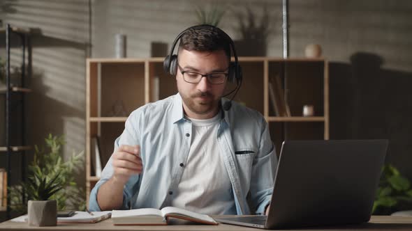 Young Man in Headphones Looking at Computer Screen Practicing Foreign Language with Teacher Online