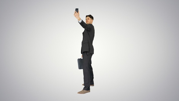 Young business man walking and taking a selfie on gradient