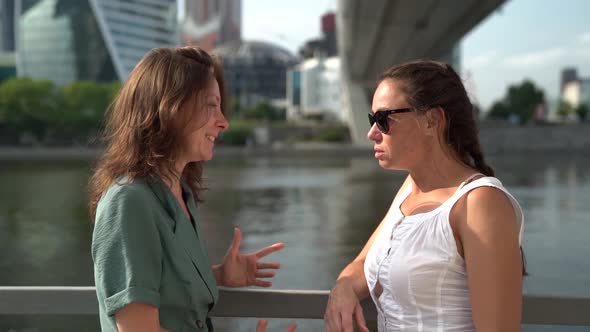 Two Women Friends Are Chatting Standing on Quay of City in Daytime, Gossiping and Talking Cheerfully