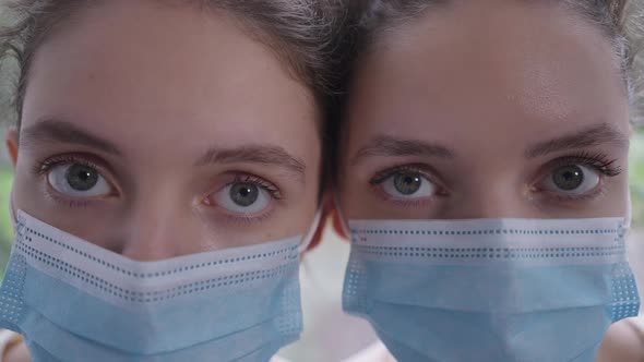 Closeup Eyes of Identical Twin Sisters in Coronavirus Face Masks Looking at Camera with Serious