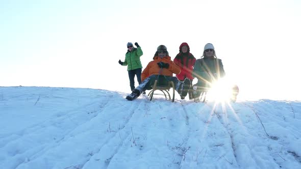 Two Senior Men Tobogganing, Wives in Background