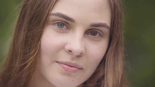 Close-up Portrait of Pretty Carefree Young Woman with Different Colored Eyes Looking at Camera