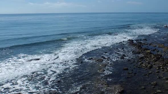 Tracking shot of a young man running on a rocky ocean beach shoreline.