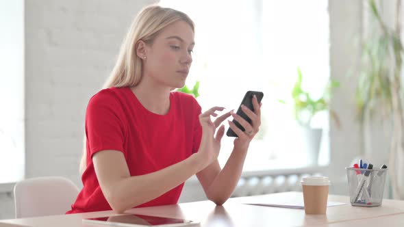 Young Blonde Woman Browsing Internet on Smartphone in Office