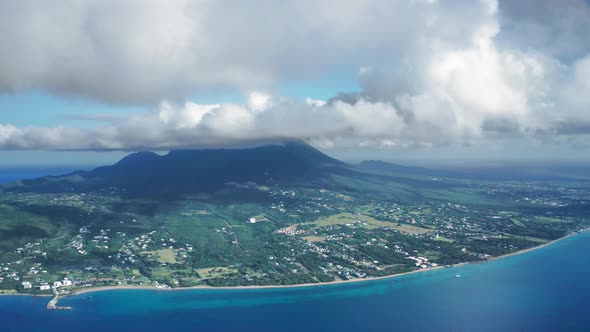 Aerial drone camera zooming Nevis Peak with the city on the coast in Saint Kitts and Nevis