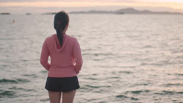 A beautiful Asian female runner looks at the sea view while standing on the beach.