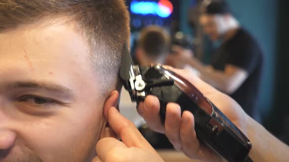 Close Up Hands of Hairstylist Cutting Hair of Young Client with Electric Razor in Barbershop. Arms