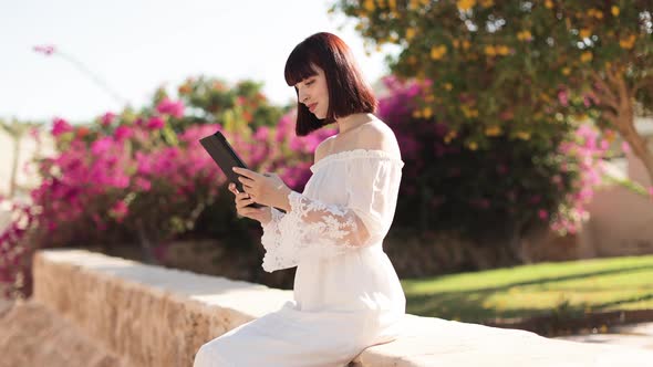 Pretty Young Girl Using Tablet While Sitting Near a Tropical Resort During Summer Vacation