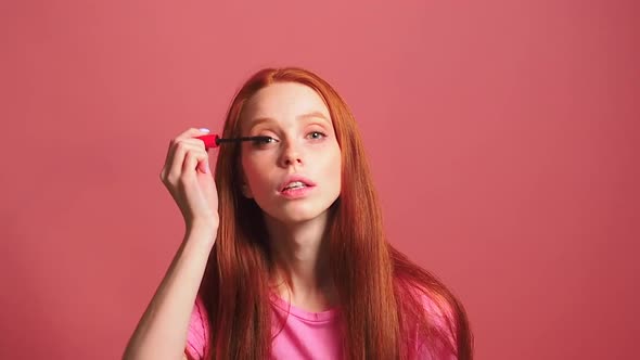 Redhaired Ginger Woman in Pink Studio Background Holding Mascara Apply on Eyeleashes Looks at Camera