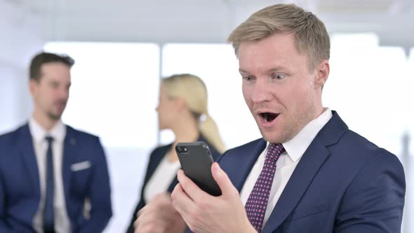 Portrait of Cheerful Businessman Celebrating Success on Smartphone 