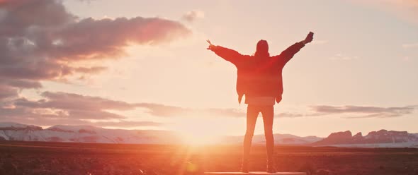 Person stands with hands outstretched while enjoying sunset
