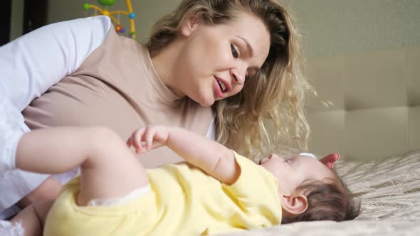 Joyful Mother with Loose Curly Hair Plays with Baby on Bed