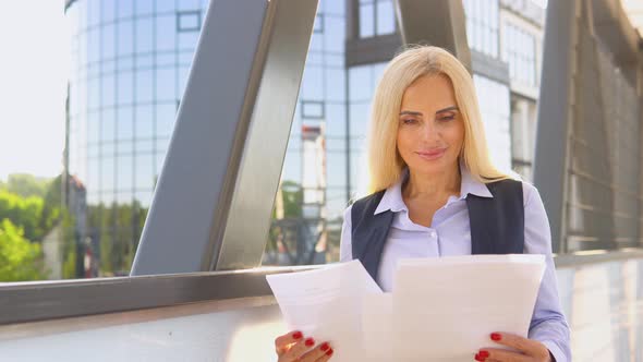 Portrait of a Confident 50 Years Woman in a Business Suit with Documents in Front of a Modern Office