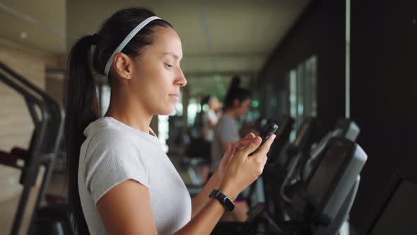 Attractive Young Mixed Race Girl Using Fitness App on Mobile Phone in the Gym. Health Sport