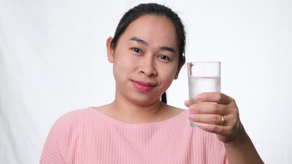 Smiling woman holding a glass of water and thumbs up on white background in studio. Healthy lifestyl