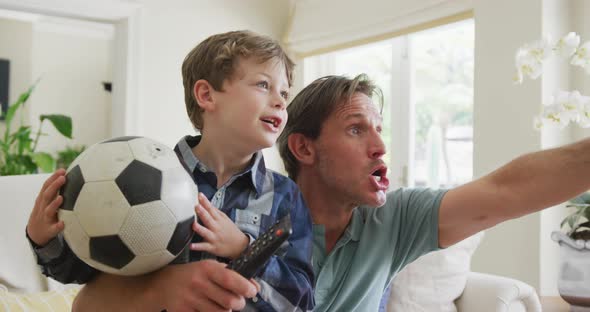 Happy caucasian father and son watching tv and supporting in living room