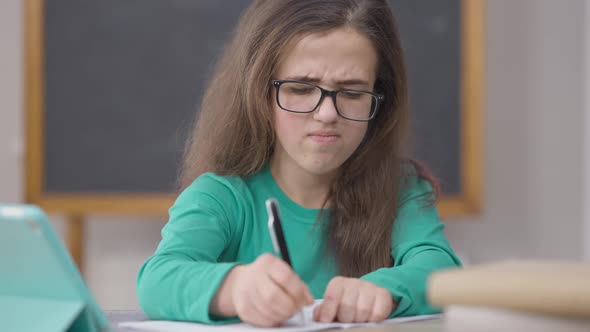 Dissatisfied University Student Writing with Pen Tearing Paper Sitting at Desk in Classroom