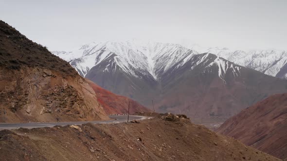 A Turn of the Road on Mountain Pass with Passing Car Against Background of Large Mountains with