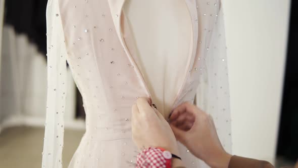 Unrecognizable Female Tailor Fasten Foundation Garment on Sparkling Wedding Dress on Mannequin in