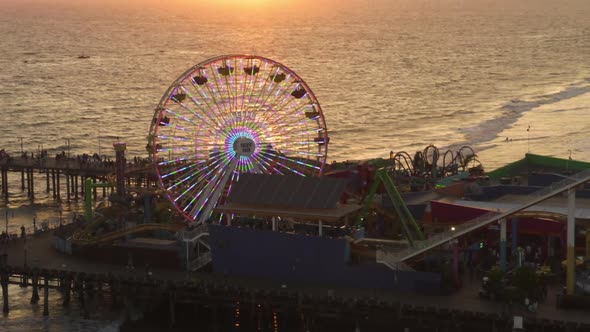 AERIAL: Close Up View of Santa Monica Pier Ferris Wheel, Los Angeles at Beautiful Sunset with