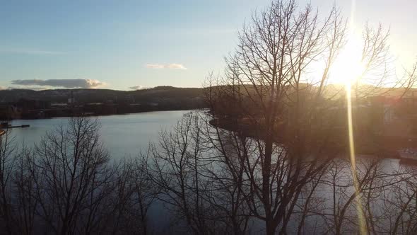 Sun glaring through trees during ascending aerial from Skien Norway - Hjellevannet lake in Telemark