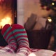 Woman feet in christmas woolen socks near fireplace decorated tree tee cup in backg - VideoHive Item for Sale
