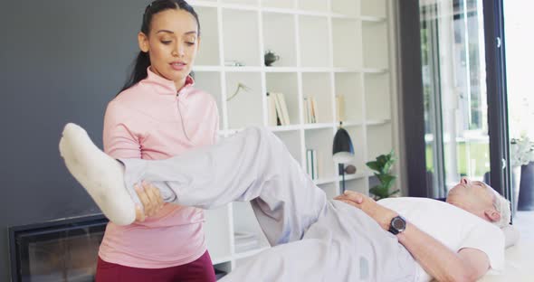 Video of happy biracial female physiotherapist exercising with caucasian senior man