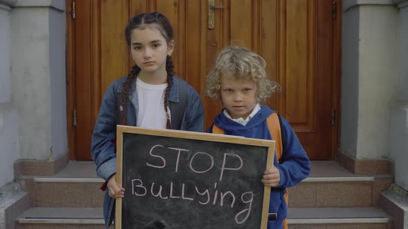 Sad Boy and Girl Looking at Camera and Holding Chalkboard with Handwritten Message Stop Bullying