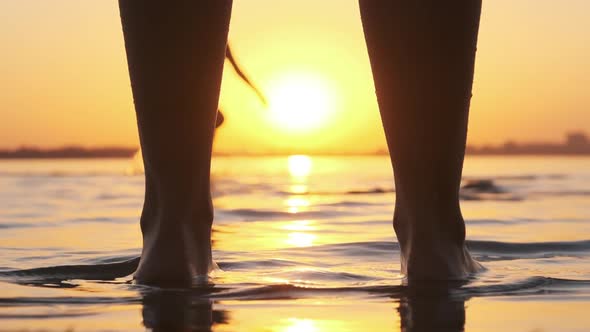 Silhouette of Woman Legs Standing in Water at Sunset on Beach. Slow Motion