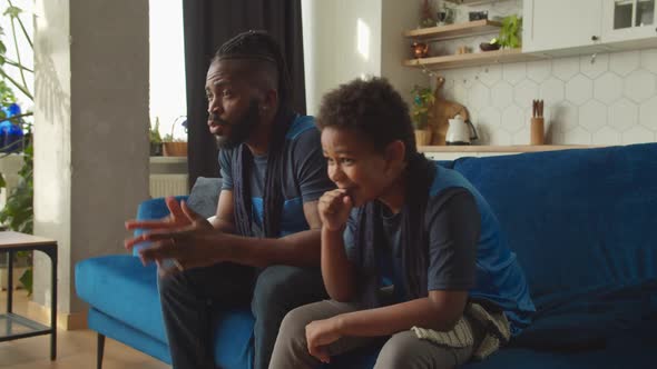 African American Son and Dad Watching Football Game on Tv Celebrating Goal