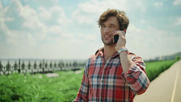 Smiling Man Talking on Smartphone Outdoors. Positive Guy Walking on Path