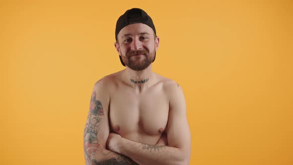 Satisfied Shirtless Bearded Tattoed Muscular Caucasian Man with Cap Standing with Crossed Arms on