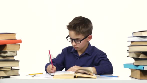 Boy Sits at a Table Recording Something Into Her Notebook and Flips Through the Book. White