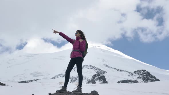 Female Climber in Sunglasses Points the Way with Her Finger Standing on a Stone Against the