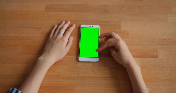 Female Hand Touching Green Mock-up Smartphone Screen Lying on Wooden Table