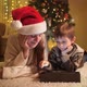 Cute Boy with Mother in Santa Hat Using Tablet Computer Next to Christmas Tree in Living Room - VideoHive Item for Sale