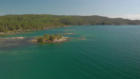 Drone panning up from sea to shore and blue sky with windmills.