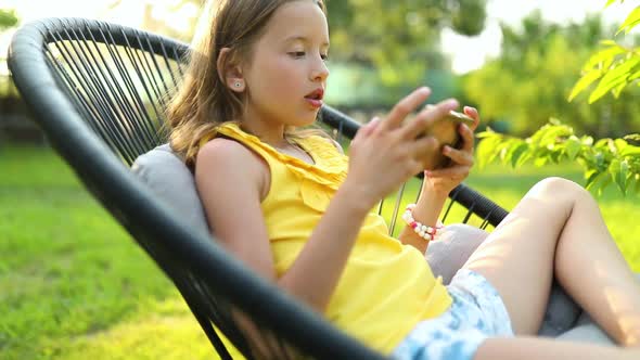 Happy kid girl playing game on mobile phone in the park outdoor