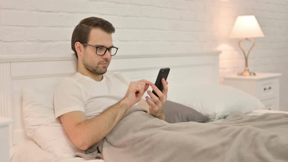 Young Man Using Smartphone in Bed