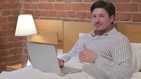 Middle Aged Man with Laptop showing Thumbs Up in Bed