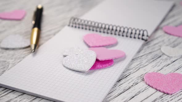 Shiny pink and white paper hearts fall on an open notebook with black metal binding.