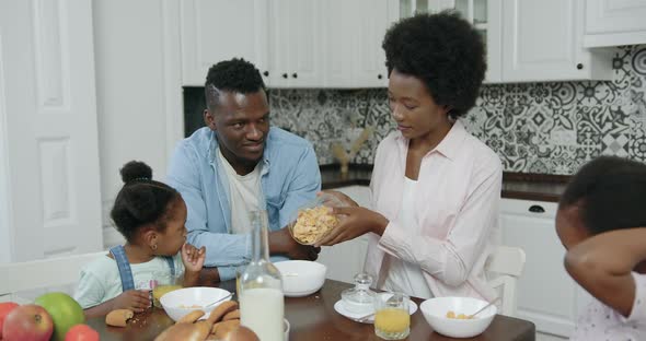 African American Couple with Small Kids Sitting at Kitchen Table and Have Breakfast 